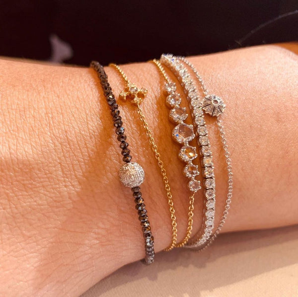 A close-up of a woman's arm adorned with a colorful stack of bracelets, highlighting a stunning aquamarine tennis bracelet.