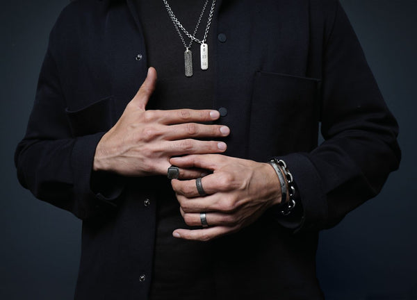A man in a black shirt with a necklace, representing contemporary style in men's wedding ring preferences.